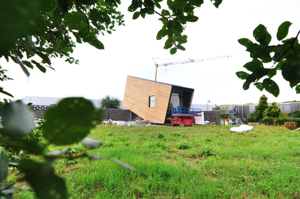 So sieht die Baustelle aus. Der schräge Klotz umhüllt die Funktionszonen des Gebäudes. Mini-Max liegt etwa 20 Kilometer nördlich vom Bodensee. Der Bürgermeister und die Gemeinde waren begeistert von der Bauidee und haben das Vorhaben begrüßt. Die Initiatorin Henrike Gänß hat in Wald ihr Abitur gemacht und parallel dazu die Tischlerausbildung absolviert.